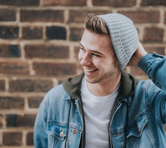 man holding the back of his head while smiling near brick wall